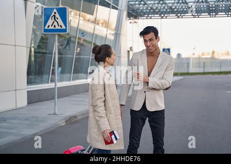 Positiver Mann, der mit dem Finger auf eine Frau mit Reisedokumenten zeigt Stockfoto