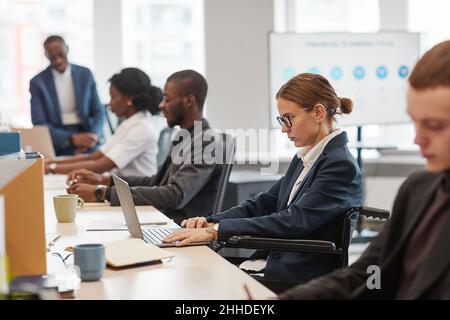 Rückansicht Porträt einer jungen Geschäftsfrau, die im Büro mit dem Rollstuhl arbeitet, während sie mit dem Computer arbeitet, Kopierraum Stockfoto