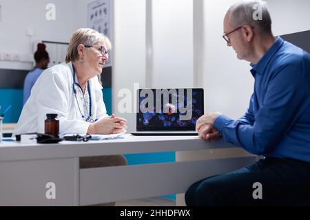 Arzt und Patient diskutieren über die Darstellung des Coronavirus auf dem Laptop. Allgemeinmediziner, der den älteren Mann mit dem Computer über die visuelle Darstellung von kovidierten 19 Bakterien erklärte. Stockfoto