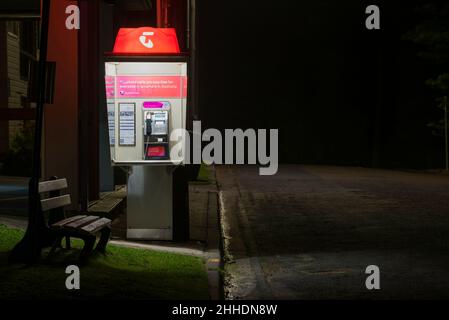 Ein öffentliches Telefon oder eine Telefonzelle von Telstra und eine Parkbank in einer dunklen Straße in New South Wales, Australien Stockfoto