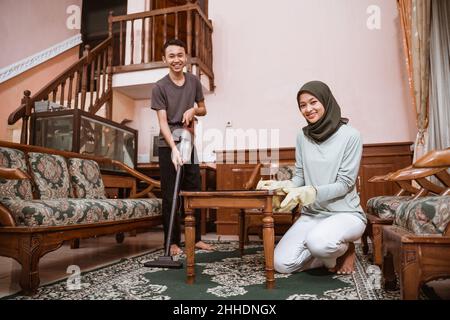 Mutter trägt Hijab und Sohn lächelt beim Putzen des Teppichs Stockfoto