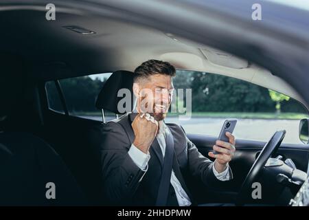 Der erfolgreiche männliche Geschäftsmann freut sich und lächelt liest Nachrichten vom Gewinn des Mobiltelefons und dem erfolgreichen Treffen, der Mann sitzt im Auto Stockfoto