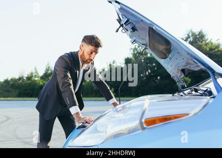 Verwirrt Mann in einem Business-Anzug untersucht den Motor des Autos Stockfoto