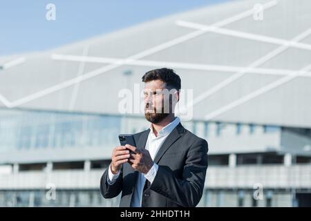 Erfolgreicher Geschäftsmann mit Bart nutzt Telefon außerhalb des Büros Stockfoto