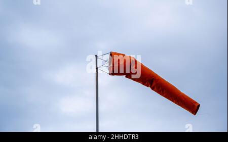 Windsocke weht auf bewölktem Himmel. Roter Kegel, Windgeschwindigkeits- und Richtungsanzeige. Windiger Tag am Flughafen. Stockfoto