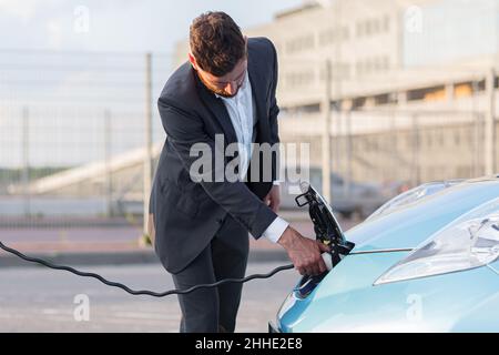 Ein Mann an einer Tankstelle lädt ein Elektroauto, ein Geschäftsmann verbindet ein Ladegerät mit einem Auto Stockfoto