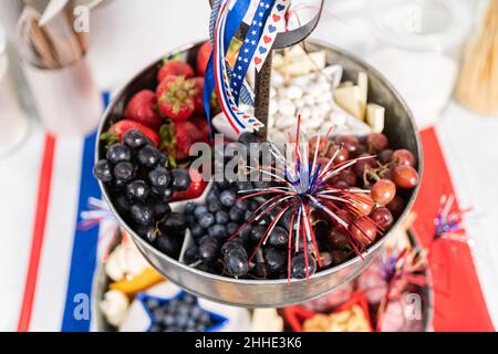 Am 4. Juli gab es ein Charcuterie-Brett auf einem zweistufigen Metallständer, gefüllt mit Käse, Crackern, Salami und frischem Obst Stockfoto