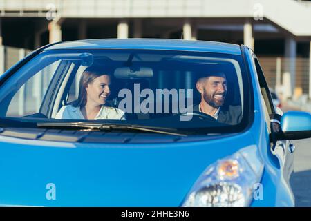 Fahrlehrer und Fahrschülerin sitzen im Auto lächelnd zusammen und lernen, ein Auto zu fahren Stockfoto