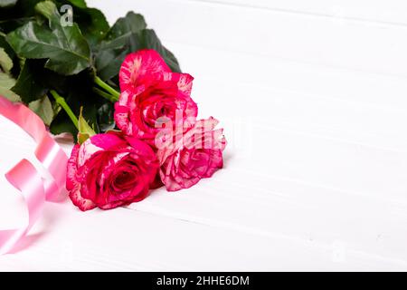 Rosen und rotes Band auf weißem Hintergrund. Das Konzept der Feiertage Stockfoto