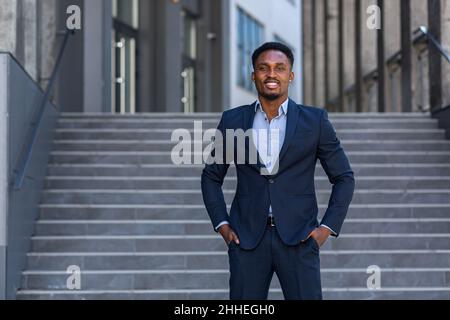 Erfolgreicher glücklicher Geschäftsmann vor dem Büro posiert und schaut Kamera afroamerikanischen Mann in Business Anzug lächelnd Stockfoto