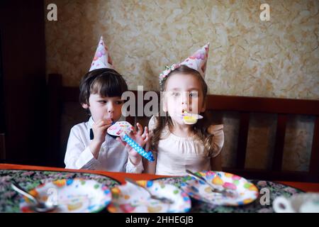 Kinderparty in Mützen feiert Geburtstag mit Kuchen und Ballons zu Hause. Stockfoto