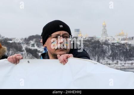 KIEW, UKRAINE - 22. JANUAR 2022 - ukrainische Flaggen werden auf die Wange eines Mannes gemalt, während einer traditionellen Menschenkettenveranstaltung auf der Patonbrücke über die Einheit D Stockfoto