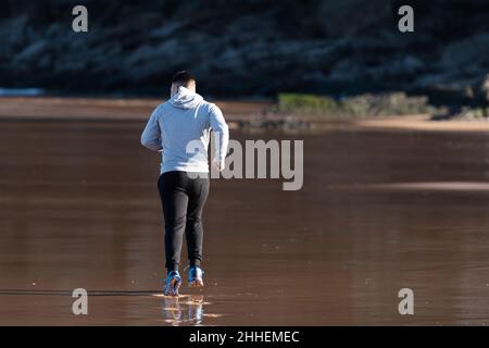 Rückansicht des Mannes mit Winterkleidung, der am Strand läuft Stockfoto