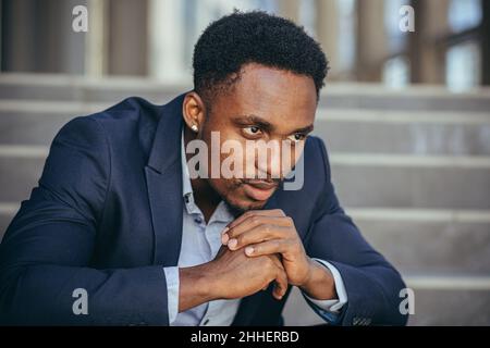 afroamerikanischer Geschäftsmann im Geschäftsanzug frustriert bekam schlechte Nachrichten von der Arbeit, feuerte depressiv auf Treppen sitzen, Nahaufnahme Porträt-Foto Stockfoto