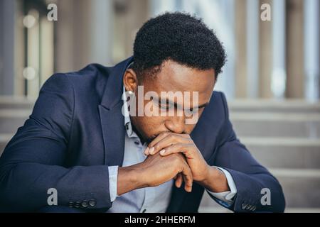 afroamerikanischer Geschäftsmann im Geschäftsanzug frustriert bekam schlechte Nachrichten von der Arbeit, feuerte depressiv auf Treppen sitzen, Nahaufnahme Porträt-Foto Stockfoto