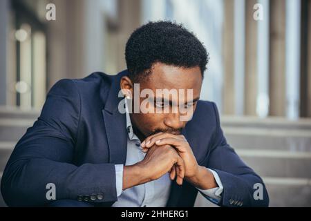 afroamerikanischer Geschäftsmann im Geschäftsanzug frustriert bekam schlechte Nachrichten von der Arbeit, feuerte depressiv auf Treppen sitzen, Nahaufnahme Porträt-Foto Stockfoto