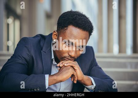 afroamerikanischer Geschäftsmann im Geschäftsanzug frustriert bekam schlechte Nachrichten von der Arbeit, feuerte depressiv auf Treppen sitzen, Nahaufnahme Porträt-Foto Stockfoto