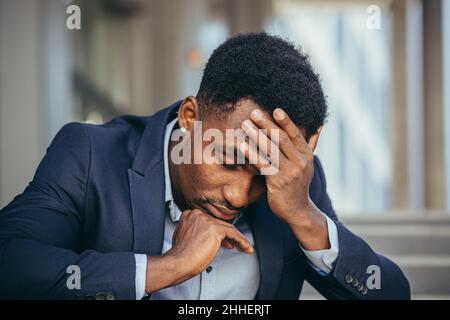 afroamerikanischer Geschäftsmann im Geschäftsanzug frustriert bekam schlechte Nachrichten von der Arbeit, feuerte depressiv auf Treppen sitzen, Nahaufnahme Porträt-Foto Stockfoto