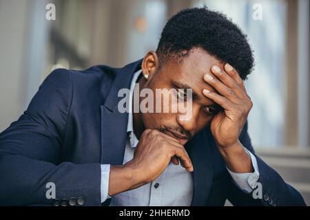 afroamerikanischer Geschäftsmann im Geschäftsanzug frustriert bekam schlechte Nachrichten von der Arbeit, feuerte depressiv auf Treppen sitzen, Nahaufnahme Porträt-Foto Stockfoto