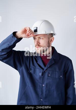 Porträt eines Bauunternehmers, Mechanikers oder Elektrikers. Serious niedlich kaukasischen bärtigen männlichen Supervisor, Vorarbeiter oder Architekt in Uniform Anpassung seiner Hut. Hochwertiges vertikales Bild Stockfoto