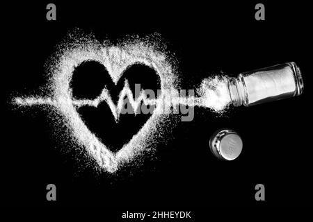 Herzförmiges Salz mit einem Kardiogramm im Inneren mit einem Salzstreuer mit bestreutem Salz. Konzept für kardiovaskuläre Probleme. Der Schaden einer erhöhten Salzaufnahme. Stockfoto