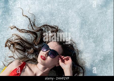 Nahaufnahme einer kaukasischen Frau, die in einer Sonnenbrille auf dem Schnee liegt. Draufsicht. Stockfoto