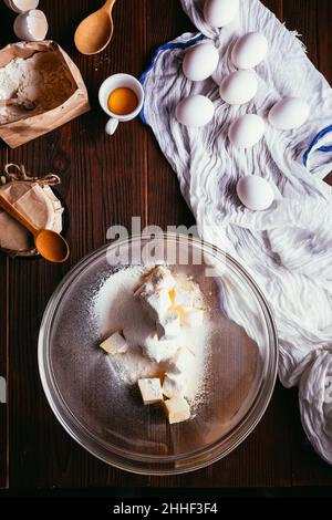 Zutaten zum Kochen Kuchen. Mehl auf gewürfelter Butter in einer Schüssel neben Eiern, Löffel und Glas Marmelade, flach legen Stockfoto