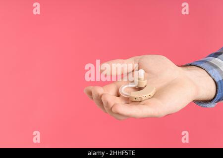 Männliches Hörgerät mit Handgriff auf rosa Hintergrund Stockfoto