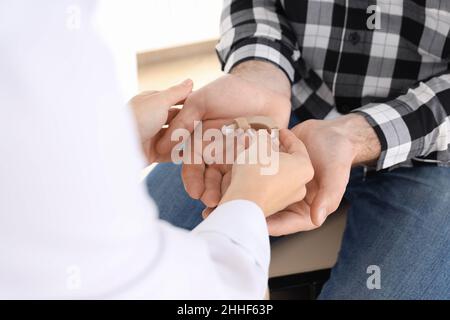 Der Arzt gibt dem Mann das Hörgerät aus nächster Nähe Stockfoto