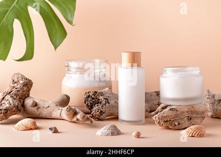 Stillleben mit wiederverwendbarer Flasche mit Scincare-Kosmetik, Feuchtigkeitspflege für das Gesicht, Gua Sha Beauty Roller auf Podien mit Muschelschalen und natürlichem Meeresdekor Stockfoto