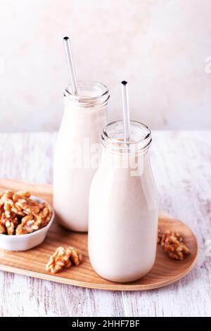 Alternative nicht milchfreie hausgemachte Walnussmilch in Glasflaschen mit wiederverwendbaren Trinkhalmen aus Metall. Walnussmilch auf Holzplatte Stockfoto