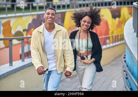 Glücklicher Mann und Frau, die Hand halten und auf der Straße spazieren gehen Stockfoto