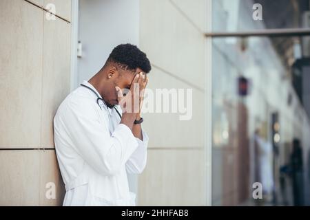 Männlicher Arzt in der Klinik hält seinen Kopf hat gesundheitliche Probleme und müde nach einem harten Tag, depressiv nicht das gewünschte Ergebnis zu bekommen, afro amerikanischen Doc Stockfoto