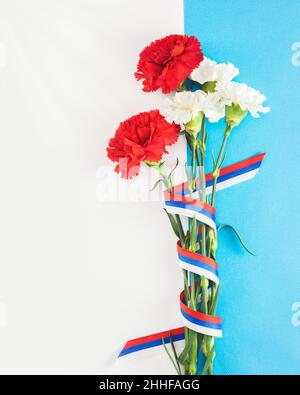 Mans Day Weihnachtskarte mit rot-weißen Nelken mit russischem Flaggenband auf weißem und blauem Hintergrund mit Kopierfläche für Glückwunschtext su Stockfoto