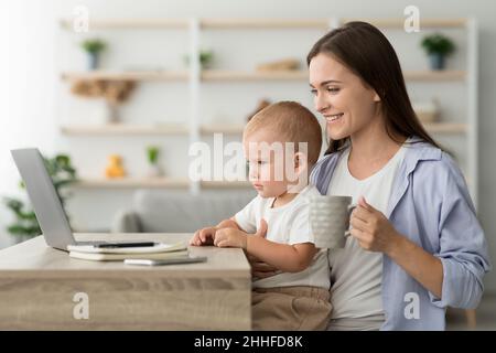 Junge Mutter Mit Kleinem Baby Trinkt Kaffee Und Benutzt Laptop Zu Hause Stockfoto