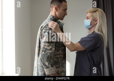 Fürsorgliche Krankenschwester, die die Hände hält und ihren militärischen Ehemann unterstützt, während sie im Krankenhaus mit ihm spricht Stockfoto