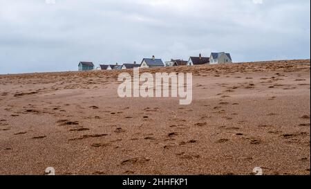 Fußabdrücke im Sand am Strand, die im November unter einem bewölkten Himmel zu den Spitzen von Holzhäusern am Strand führen Stockfoto