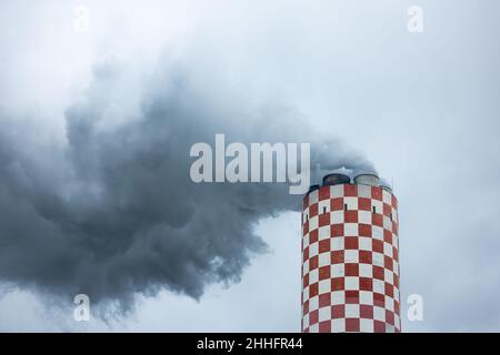 Aus dem Kamin eines Kohlekraftwerks kommen dichte Rauchwolken. Aufnahme an einem bewölkten Tag, gleichmäßiges und weiches Licht. Stockfoto