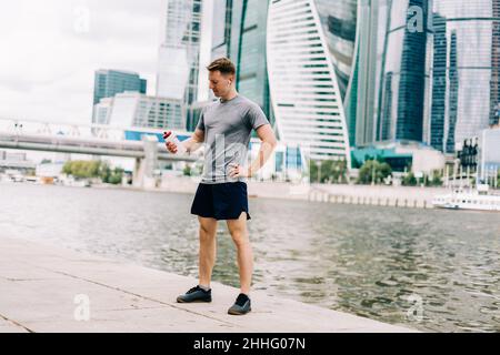 Müder junger Läufer trinkt Wasser und entspannt sich nach dem Sporttraining. Halten Sie eine Wasserflasche während des Fitnesstrainings in der städtischen Straße der Sommerstadt Stockfoto