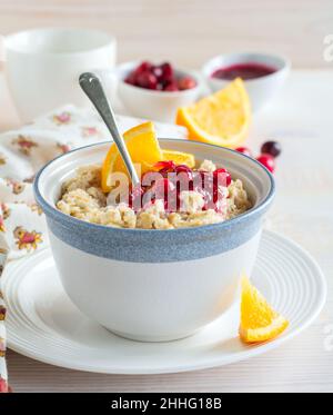 Haferbrei mit Cranberry-Sauce und Orange in einer Keramikschale für ein gesundes Frühstück auf hellem Hintergrund. Selektiver Fokus. Stockfoto