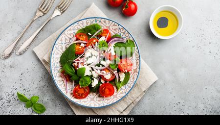 Tomaten, Spinatblätter, rote Zwiebeln und Feta-Käse-Salat auf hellem Keramikplatte auf grauem Hintergrund. Selektiver Fokus. Draufsicht. Stockfoto