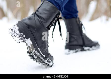 Weibliche Beine in schwarzen Leder Schnürstiefeln auf Schnee. Frau, die auf der Winterstraße läuft, warme Schuhe für kaltes Wetter Stockfoto