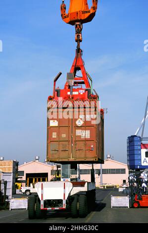 Transportbehälter über LKW im Hafen aufgehängt. Kran bewegt einen Frachtcontainer. Ladebereich für kommerzielle Rampen. Infrastruktur USA Stockfoto