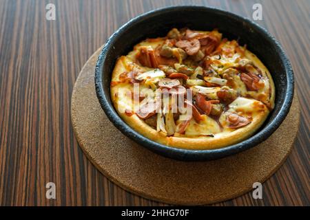 Barbeque-Pizza-Hütte mit Rind, serviert auf einem schwarzen Teller oder einer Schüssel mit einem braunen strukturierten Holztisch im Hintergrund. Gewürzte Bratkartoffeln auf einem weißen Teller serviert. Stockfoto
