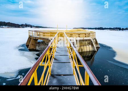 Damm auf dem gefrorenen Fluss. Blick auf den im Winter mit Eis bedeckten Staudamm. Stockfoto