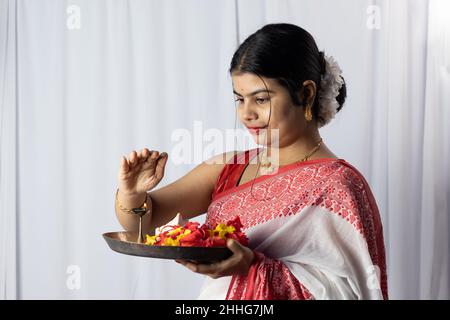 Eine wunderschöne indische Frau in rotem Saree, die Puja thali oder eine Gebetstafel auf weißem Hintergrund hält Stockfoto