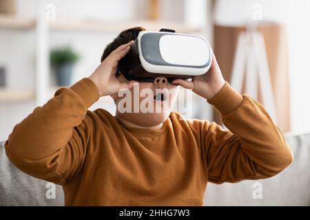 Staunend molliger Junge mit VR-Brille, häusliche Innenausstattung Stockfoto