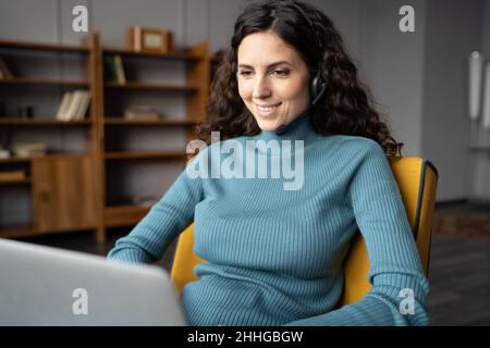 Lächelnde, selbstständige Freiberuflerin in einem schnurlosen Headset mit Mikrofon für Online-Konsultationen Stockfoto