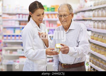 Die Fragen aus der Medikation herausnehmen. Aufnahme eines jungen Apothekers, der einem älteren Kunden hilft. Stockfoto