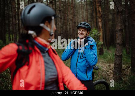 Ältere Biker, die am Herbsttag im Wald im Freien Fahrradhelm aufsetzen. Stockfoto
